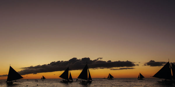 Silhouette sailboats sailing on sea against sky during sunset