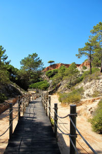 Footpath by railing against blue sky