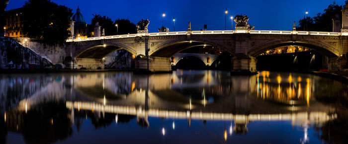 Reflection of bridge on river against sky in city at night