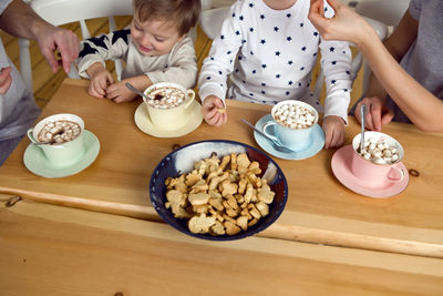 Parents feed children cookies and coffee sitting at the table in the kitchen