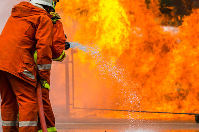 Rear view of firefighter spraying water on fire while standing at street