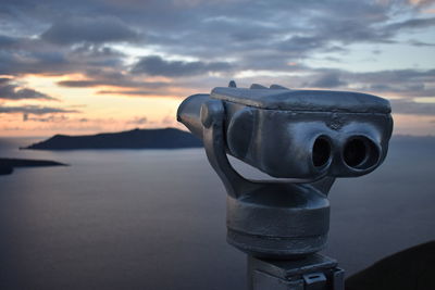 Close-up of coin-operated binoculars by sea against sky during sunset