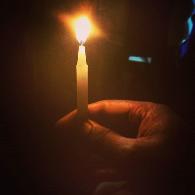 CLOSE-UP OF HUMAN HAND HOLDING LIT CANDLE IN THE DARK