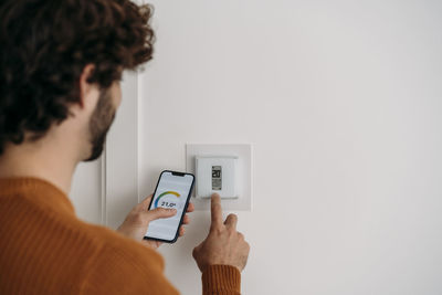 Young man operating thermostat with smart phone at home