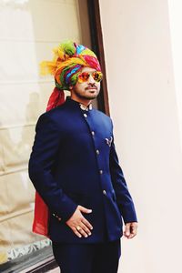 Indian man standing in multi colored turban against white wall  in blue dress