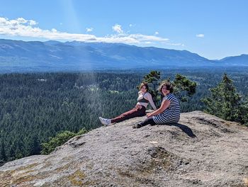 Sisters sitting on the edge of a cliff overlooking the trees.