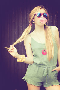 Beautiful young woman posing while blowing bubble gum against wall