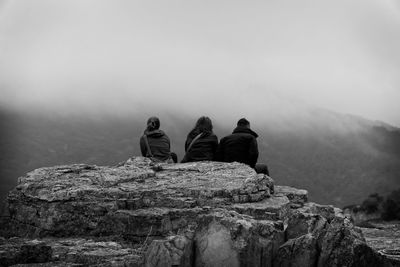 Rear view of friends sitting on rock against mountain