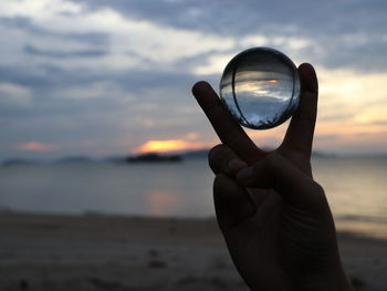 Close-up of hand holding sea against sunset sky