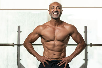 Portrait of shirtless man with hand on hip standing in gym