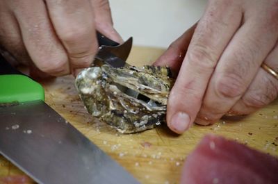Cropped image of man breaking oyster shell on cutting board