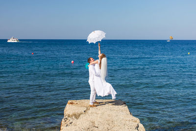 Woman standing on rock by sea against sky