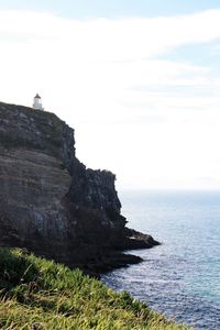 Man sitting on rock by sea against sky