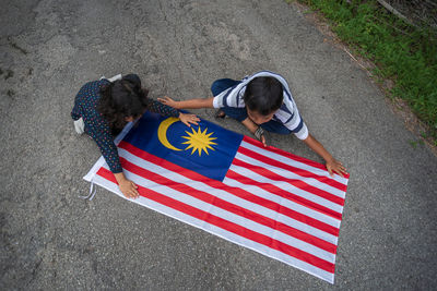 High angle view of friends playing with malaysian flag on road