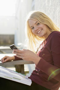 Portrait of happy high school girl holding mobile phone at picnic table