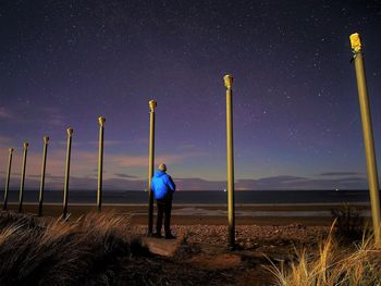 Rear view of man standing on field against sky at night