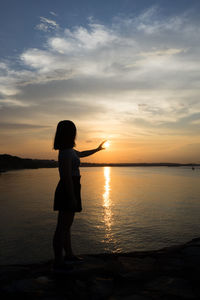 Silhouette woman standing on beach against sky during sunset