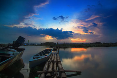 Sailboats moored in lake against sky during sunset