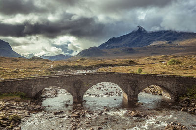 Arch bridge over river against mountains