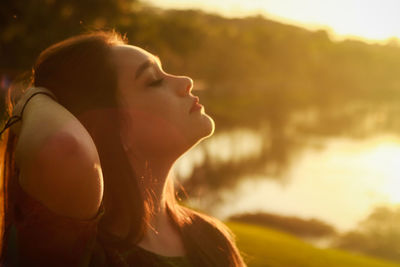 Beautiful woman standing by lake on field during sunset