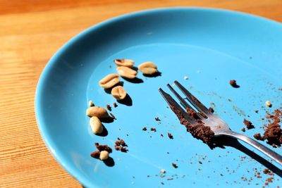 A blue plate with a chocolate brownie leftover and peanuts on a wooden table