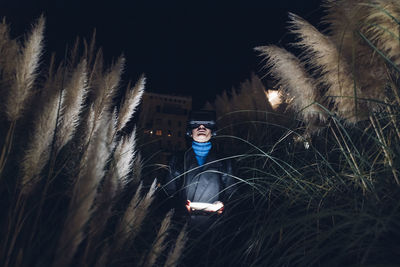 Businesswoman with virtual reality headset amidst grass at night