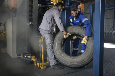 Two tire repairmen lifting tire in factory