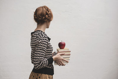 Woman holding book while standing against wall