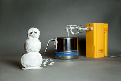 Snowman made with cream by grinder and container against gray background