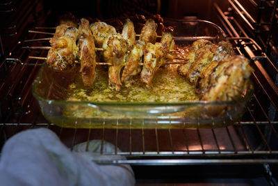 Hand with glove taking out of the oven a glass tray with chicken wings roasted in a healthy way