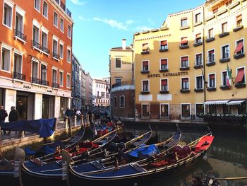 Boats moored on canal in city against sky