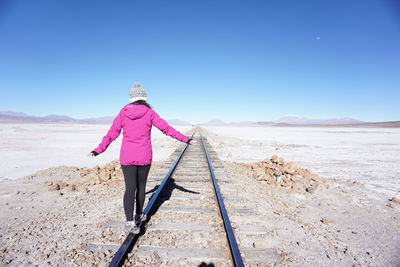 Rear view of woman standing on rails against clear sky