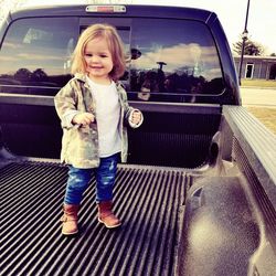 Portrait of happy girl standing on car