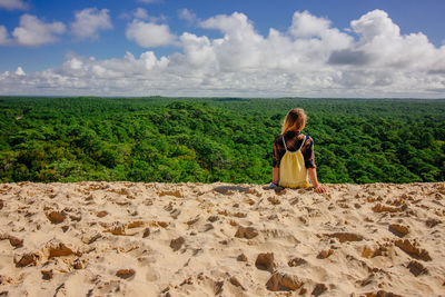 Rear view of woman sitting on sand against forest