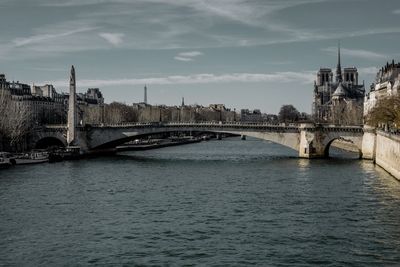 Bridge over river in city against cloudy sky