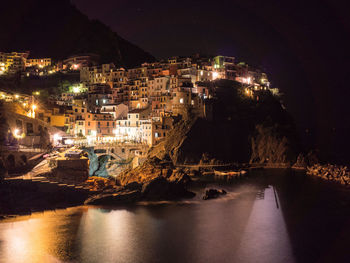 Illuminated buildings by sea against sky at night in vernazza