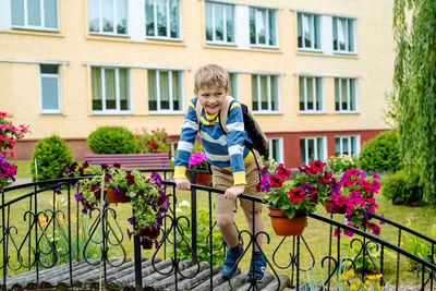 Full length of boy standing on footbridge by flower against school building