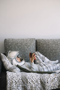 Adorable kid wearing pajama while sitting on couch. he is lying on couch while playing with a video game console at home