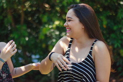 Smiling young woman standing by friend against trees