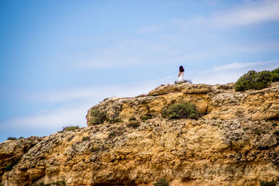 Woman standing on rock formation against sky