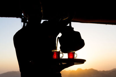 Silhouette man pouring black tea at shop during sunset