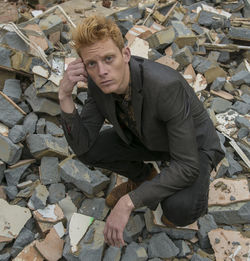 Portrait of young man crouching on broken wall