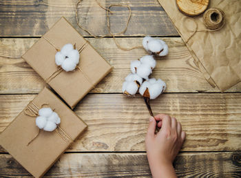 Women's hands hold a box on a wooden background.the decor is made of cotton flowers.