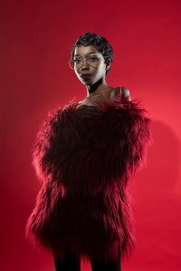 Young woman wearing eyeglasses and fur clothing standing against red background