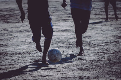 Low section of people playing soccer on beach