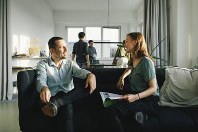 Businessman discussing with female colleague while sitting on sofa at office