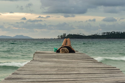 Woman sitting on pier over sea against sky