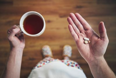 Sick man in nightwear is taking pills and cup of  tea. 