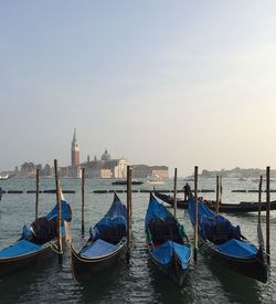 Gondolas moored in canal against sky during sunset