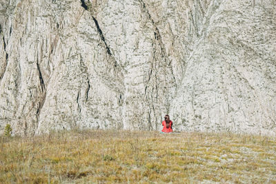 Small figure of young woman in red traveler back on mountais rock background